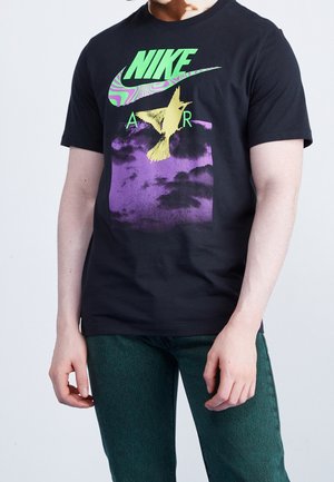 Schwarzes T-Shirt mit einem bunten Nike-Logo, einer gelben Vogelgrafik und einem lila Hintergrund mit Wolkenmustern. Kurze Ärmel und Rundhals.