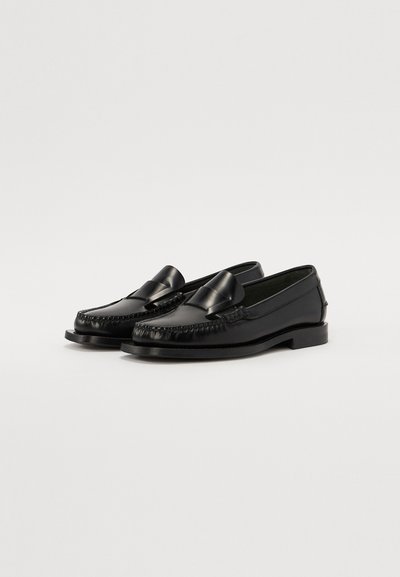Mocassins en cuir noir avec un bord tissé décoratif et un accent en nœud sur le devant, dotés d'une semelle plate et d'une finition lisse.