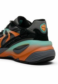 Melni un pelēki sporta apavi ar oranžiem un teal akcentiem. Iezīmējas ar teksturētu augšpusi, raksturīgu viļņveida zoli un redzamu zīmolu uz papēža.