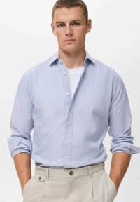 Himmelblau- und weiß gestreiftes Langarmhemd mit Button-Down-Kragen und hochgekrempelten Ärmeln, kombiniert mit beigen Hosen. Glatte Stofftextur.
