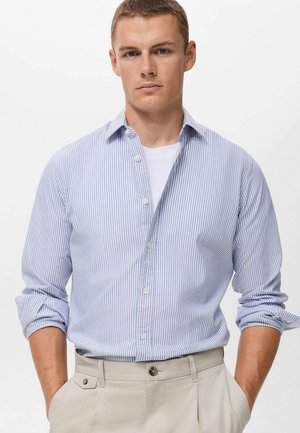 Light blue and white striped long-sleeve shirt with button-down collar and rolled-up sleeves, paired with beige trousers. Smooth fabric texture.