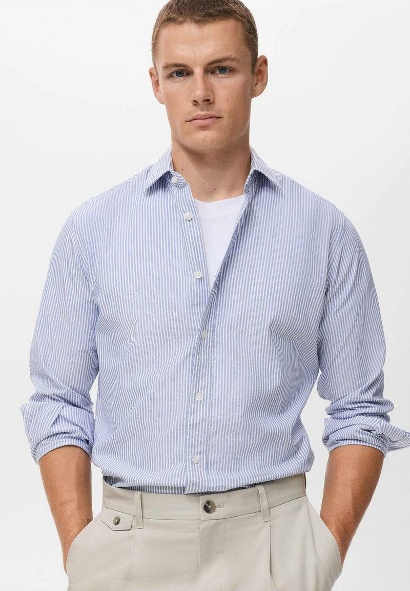 Himmelblau- und weiß gestreiftes Langarmhemd mit Button-Down-Kragen und hochgekrempelten Ärmeln, kombiniert mit beigen Hosen. Glatte Stofftextur.