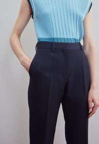 Jasnoniebieska, strukturalna bluzka bez rękawów z geometrycznymi wzorami, zestawiona z granatowymi spodniami o dopasowanym kroju, z bocznymi kieszeniami i płaskim przodem.