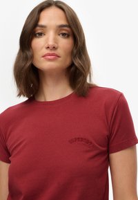 Bordeaux katoenen t-shirt met korte mouwen, voorzien van een verhoogd, geborduurd "Superdry" logo op de borst en een klassieke ronde hals.