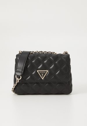 Black quilted leather crossbody bag with gold chain strap and triangular Guess logo plaque on front flap.