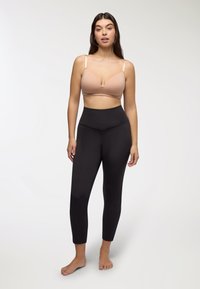 Soutien-gorge beige chiaro con spalline regolabili e scollatura a V abbinato a leggings neri a vita alta, texture liscia e lunghezza alla caviglia.