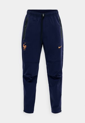 Marineblå avsmalnende treningbukser med elastisk linning, sidelommer med glidelås, oransje Nike-logo og det franske fotballforbundets logo med to stjerner.