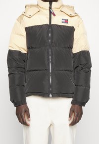 Puffjacka med dragkedja, med en krämfärgad övre del och svart nedre del, framträdande logotyp patch och avtagbar huva.