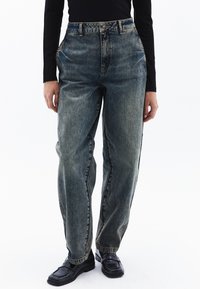 Jeans de tiro alto y corte holgado en denim azul desgastado, con cierre de botón, trabillas para cinturón y bolsillos laterales. Diseño simple de pierna recta.