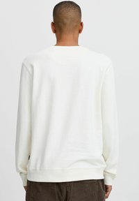 White crew neck sweatshirt with long sleeves, soft texture, and a relaxed fit. Features ribbed cuffs and hem, plain design without patterns.