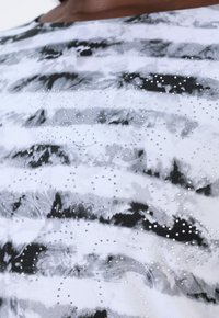 Schwarz-weißer gewirkter Oberteil mit einem Batik-Effekt, verziert mit verstreuten Strasssteinen und einem weichen, strukturierten Stoff.