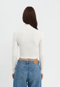 Hvit avkortet langermet topp med høy hals, kombinert med høytlivede blå denimjeans med klassiske lommer og sømdetaljer.