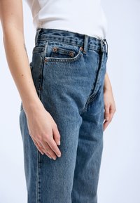 Hogwaist blauwe denim jeans met een lichte vervaging, voorzien van een vijf-pocket ontwerp en koperen hardware. Gelaagd stof met zichtbare stiksels.