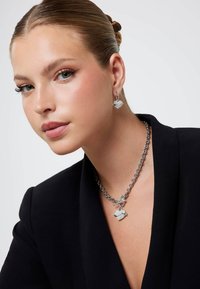 Srebrny zestaw biżuterii z zawieszką w kształcie serca na masywnym łańcuszku oraz pasującymi kolczykami, oba ozdobione misternymi detalami.