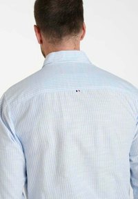 Blauw gestreept shirt met een kraag, knopen aan de achterkant en een klein driekleurig embleem bij de achterkant van de halslijn. Gestructureerde katoenen stof.
