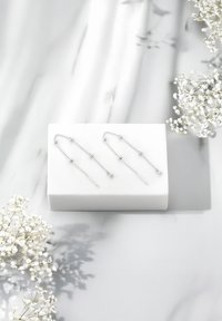 Boucles d'oreilles en argent avec un design en chaîne, comportant des perles rondes et des accents droits, présentées sur une boîte blanche sur un fond en marbre.