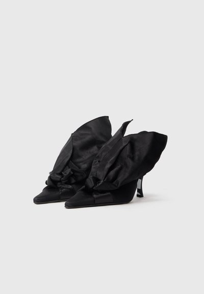 Sapatos de cunha pretos com bico pontiagudo e sobreposição de tecido assimétrica que se assemelha a asas. Feitos de cetim com uma textura elegante e suave.