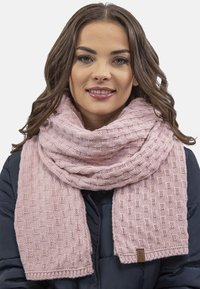 Sciarpa rosa lavorata a maglia con un motivo testurizzato, forma ampia, bordi rifiniti e un piccolo etichetta marrone a un'estremità, indossata sopra un giubbotto scuro.