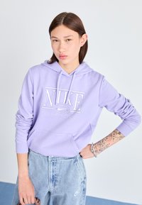 Hoodie violet clair avec un logo Nike blanc bien en évidence et le texte "SPORTSWEAR". Le tissu semble doux avec une poche kangourou à l'avant.