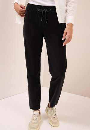 Pantalon de jogging léger noir avec une taille élastique, un cordon de serrage, des poches latérales et une coupe fuselée, associé à des baskets crème.