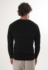 Schwarzer Strickpullover mit langen Ärmeln und rundem Ausschnitt, mit Rippstruktur und eingesetzten Schultern, von hinten betrachtet.