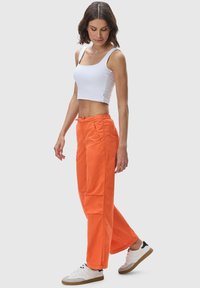 Orange cotton pants with a relaxed fit and drawstring waist, paired with a white cropped tank top and white sneakers.