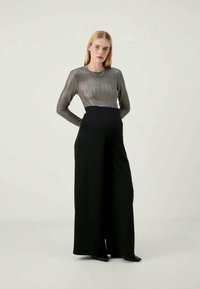 Top lung cu mânecă lungă de un argintiu metalic, cu dungi verticale, asortat cu pantaloni largi negri, cu talie înaltă. Texturi fine și linii curate.