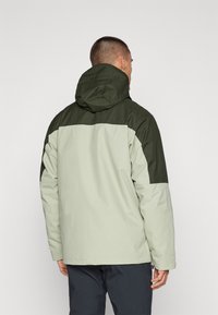 Veste à capuche vert clair et vert foncé avec un design bicolore. Fabriquée en matériau lisse et résistant à l'eau, avec une coupe décontractée.