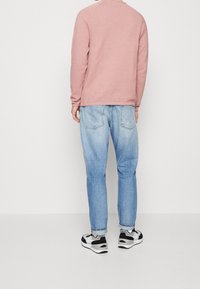 Jasnoróżowy sweter z długimi rękawami w połączeniu z wyblakłymi niebieskimi dżinsami. Białe i czarne sneakersy dopełniają casualowy wygląd.