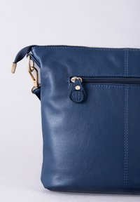 Navy leather bag with a zippered closure, featuring a front pocket and gold-tone hardware. Smooth texture with a minimalist design.