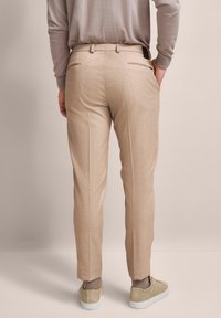 Beige maßgeschneiderte Hose mit Slim Fit, mit seitlichen Taschen, Gesäßpaspeltaschen und glatter Stoffstruktur. Dazu leichte Schuhe.