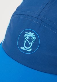 Zils cepure ar zilu izšūtu simbolu, uz kuras attēlots karikatūru tēls, izgatavota no gludas, vieglas auduma. Malu šuvju detaļas.