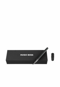Melnā lodīšu pildspalva ar teksturētu rokturi, sudraba detalizējumiem un atbilstošu melnu kastīti, kurā ir uzraksts "Hugo Boss" baltā krāsā.
