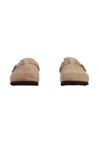Chaussures slip-on en suédine beige clair avec deux sangles à boucle réglables, dotées d'une semelle en caoutchouc foncé et d'un design minimaliste.