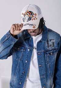 White trucker cap with embroidered geisha and floral design; denim jacket with button closures; black “13” detail on the chest.