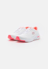Zapatillas deportivas blancas con parte superior de malla, acentos rosas en la lengüeta y la suela, cuello acolchado y suela exterior de goma flexible.