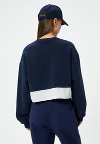Sudadera corta navy con panel inferior blanco, mangas largas, cuello acanalado y hombros instalados, combinada con pantalones navy a juego.