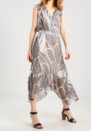 Mouwloze midijurk met bruin-witte bladprint, V-hals, getailleerde taille en asymmetrische zoom gedragen met zwarte sandalen met hak en enkelbandje.