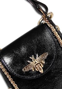 Sac en cuir noir avec une texture brillante, orné d'un emblème de abeille en ton doré sur le rabat et d'une bandoulière en chaîne dorée.