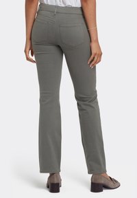 Pantalones grises de campana con una textura suave, cintura alta y dos bolsillos traseros. Llevados con zapatos de tacón topo, que enfatizan la longitud y el ajuste.