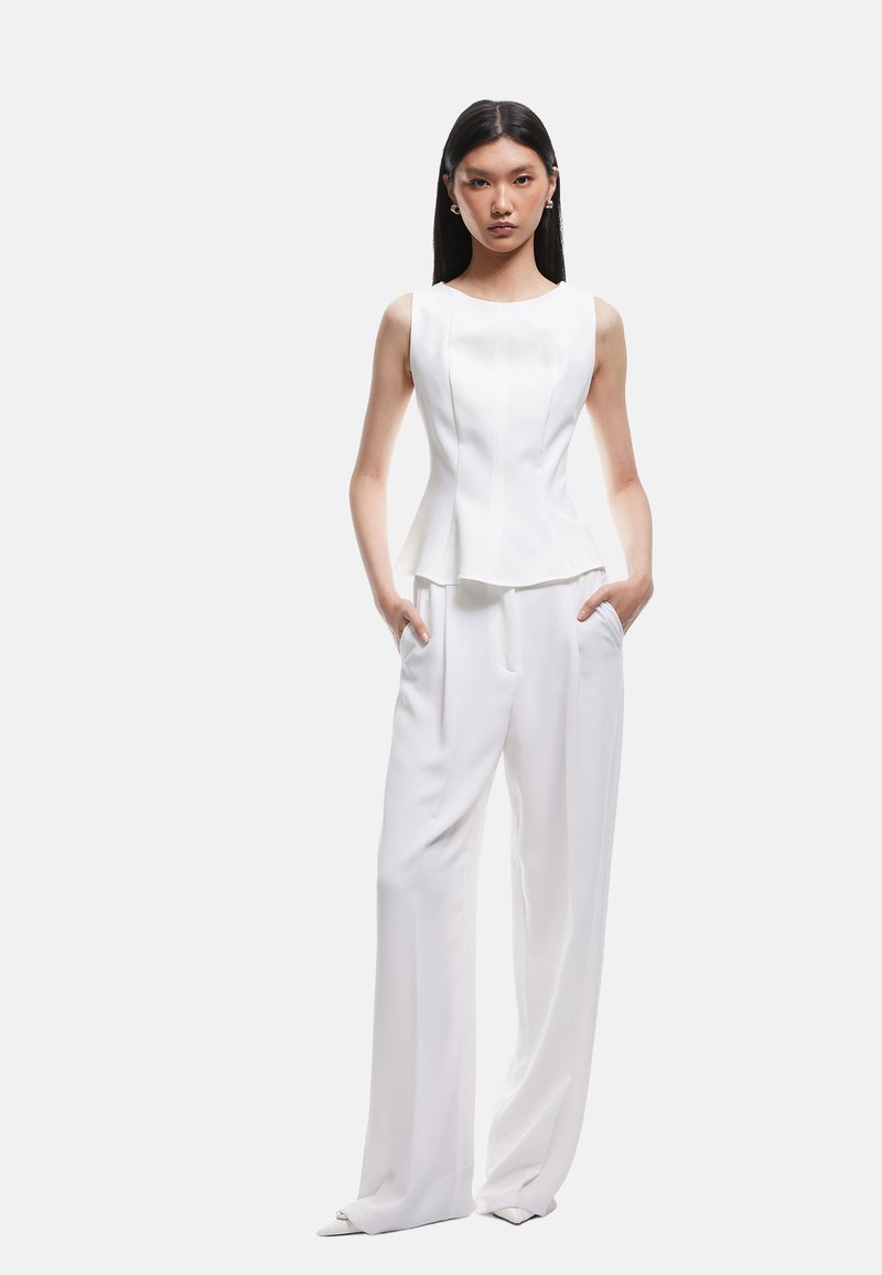 Witte mouwloze top met een getailleerde silhouet en een peplum taille, gecombineerd met losse witte broek met zijzakken. Glad, lichtgewicht stof.