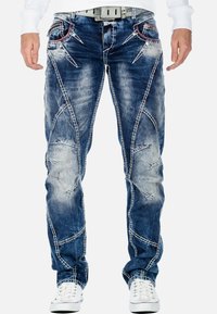 Jeans in denim blu con toppe strappate, cuciture bianche a contrasto e un design affusolato. Presentano tasche anteriori con cuciture di accento.