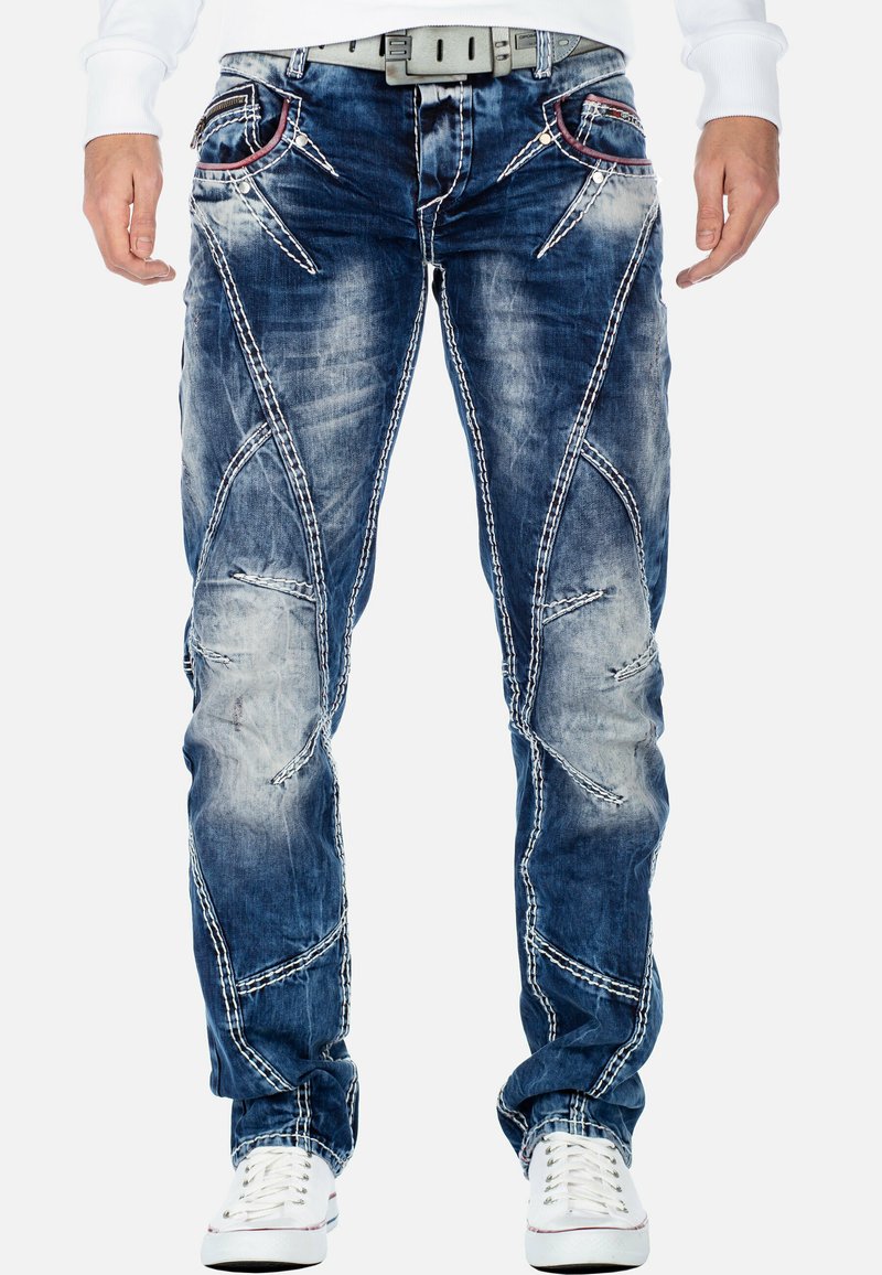 Jeans in denim blu con toppe strappate, cuciture bianche a contrasto e un design affusolato. Presentano tasche anteriori con cuciture di accento.