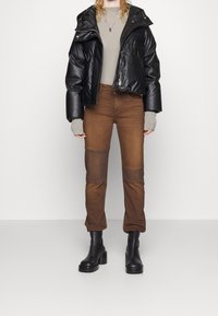 Chaqueta acolchada negra con un diseño ajustado, mangas largas y cremallera; suéter gris de punto acanalado debajo; jeans marrones con detalles de parches; botas negras gruesas.