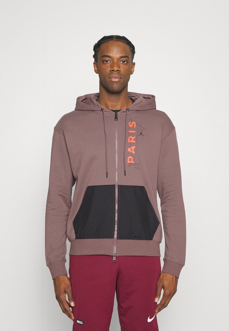 Marsala hoodie med sorte detaljer og kengurulomme, med teksten "PARIS" i orange, lynlås lukning og snoretræk. Blød stoftekstur.