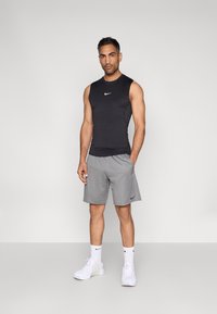 Μαύρο αθλητικό μπλουζάκι χωρίς μανίκια, γκρι σορτς, λευκά αθλητικά παπούτσια και κάλτσες με μαύρες λεπτομέρειες. Απλός σχεδιασμός, εφαρμοστή γραμμή και λεία υφή.