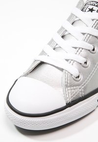 Silberne Ledersneaker mit einer weißen Gummikappe, schwarzem Rand und weißen Schnürsenkeln. Ausgestattet mit Metallösen und strukturiertem Obermaterial.