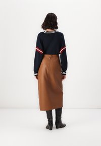 Maglione navy con righe rosse e bianche sulle maniche, abbinato a una gonna midi in pelle marrone. Stivali neri con tacco completano l'outfit.