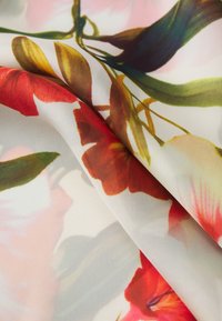 Tessuto a stampa floreale con vivaci fiori rossi e rosa su uno sfondo chiaro, caratterizzato da una consistenza liscia e trasparente e un design fluido.