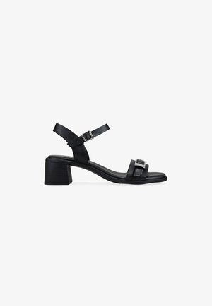 Sandalia de cuero negro con tacón de bloque de 5 cm, tira ajustable en el tobillo y detalle de hebilla en la tira del dedo, mostrada sobre fondo blanco.